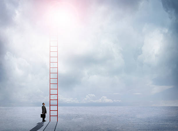 istock Businessman Looks Up At Red Ladder Extending Into The Clouds 519364332