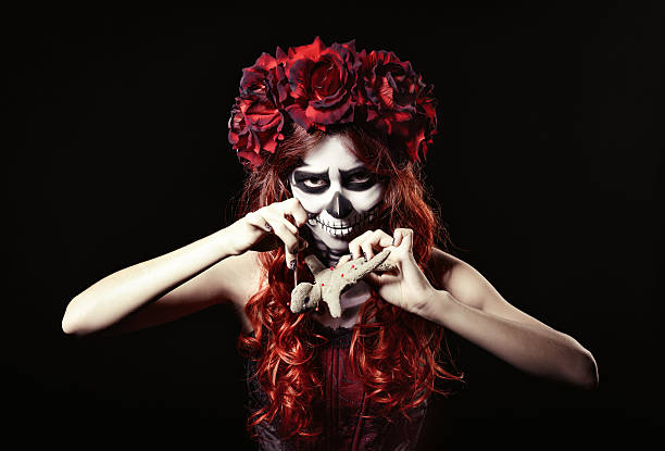 istock Young voodoo witch with muertos makeup (sugar skull) piercing doll 519364445