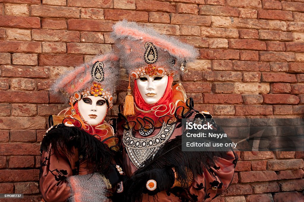 Venice Carnival 2014 Venice, Italy - February 24, 2014: The photo was taken al Arsenale in Venice, Italy during the famous Venice carnival. Masked couple wearing traditional carnival costume with fur cap. Thay posing against brick wall. Venice, Italy. 2014 Stock Photo