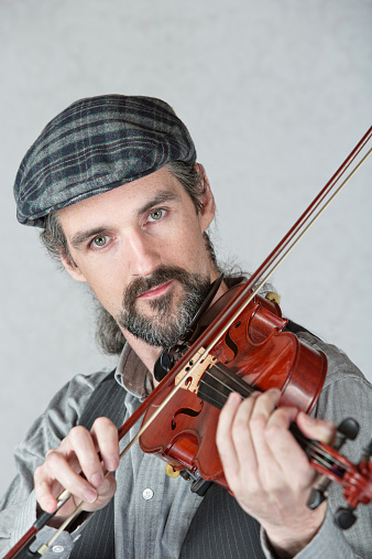 Serious Irish man playing a fiddle over gray background