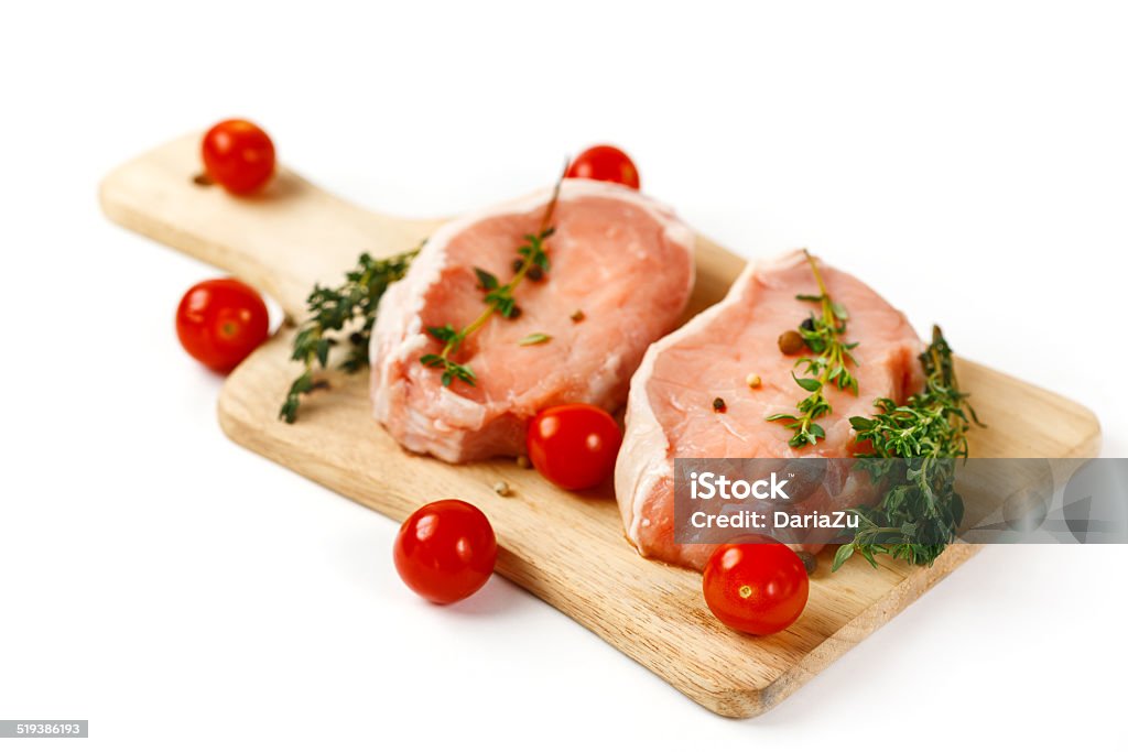 Fresh raw pork steaks on cutting board Fresh raw pork steaks on cutting board serving with cherry tomatoes and herbs. Over white background, selective focus. Barbecue - Meal Stock Photo