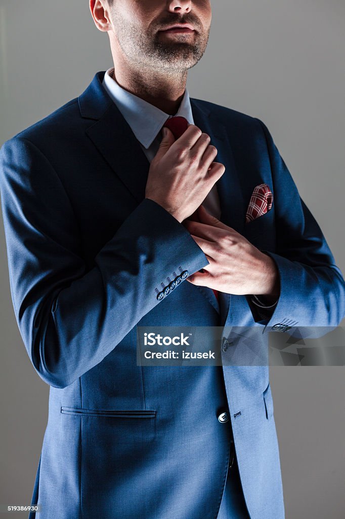 Elegant businessman wearing suit Portrait of elegant businessman wearing suit and pocket square. Standing against dark grey background. Close up of torso and hands. Adult Stock Photo