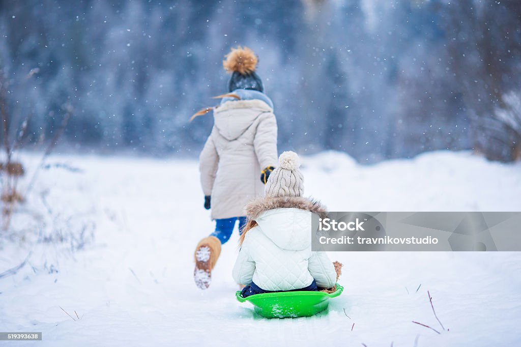 Little adorable girls enjoy a sleigh ride. Child sledding Adorable little happy girls sledding in winter snowy day. Family vacation on Christmas eve outdoors Sledding Stock Photo