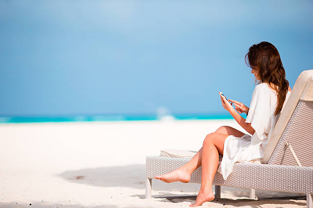 junge frau auf liegestuhl mit mobiltelefon am strand - sand river stock-fotos und bilder