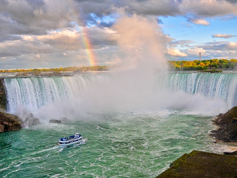 Dramatic view of a rainbow formed in the mist and storm clouds over Niagara Falls.  Tour boat is in the mist under the falls.