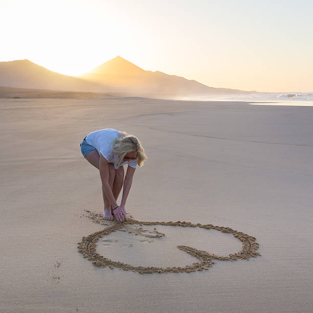 istock Lady drawing heart shape in sand on beach. 519402138