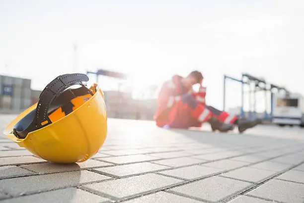 Photo of Yellow hardhat at shipyard with depressed male worker in background