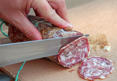 Cook's hand slicing the salami with a knife-sharp