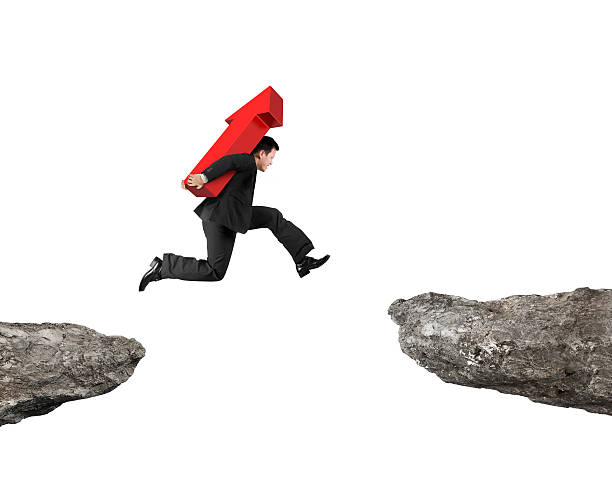 istock Man carrying red arrow sign jumping over two cliffs 519420724