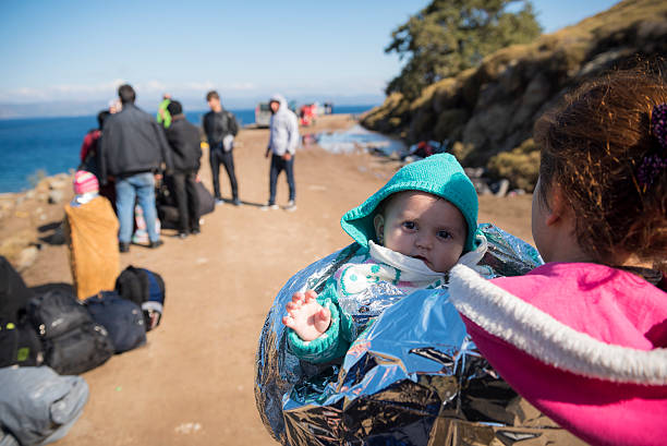 Lesbos, Greece - October 25, 2015: Ala, 10 months old and from Qamishli, Syria, is wrapped in a foil blanket after reaching the coast of Lesbos at the end of a dangerous boat ride from Turkey. The family is Kurdish. Other refugees are in the background.