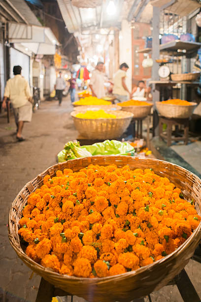 Marigolds for Sale at a Flower Market, Mumbai, India Baskets of bright orange and yellow marigolds ready to be threaded into garlands for sale at a neighbourhood covered flower market in Mumbai, India.  Shoppers and vendors in the background. flower market stock pictures, royalty-free photos & images