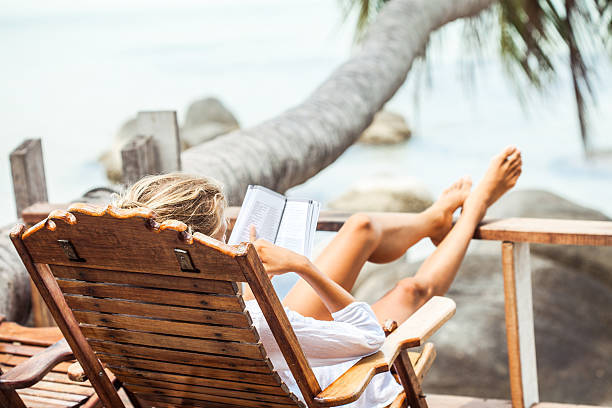 istock Young woman reading a book while relaxing on tropical island 519426472