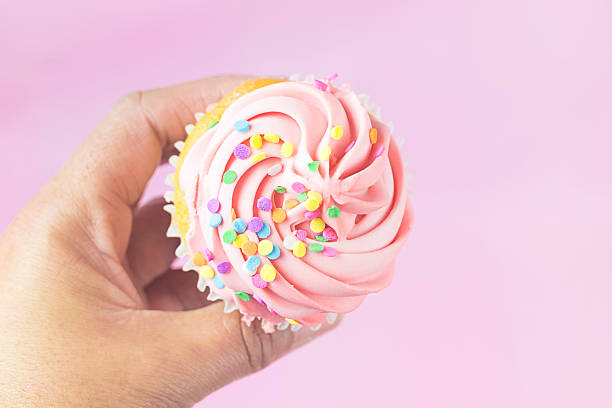 istock Hand Holding Pink Iced Cupcake with Pastel Sprinkles 519432376