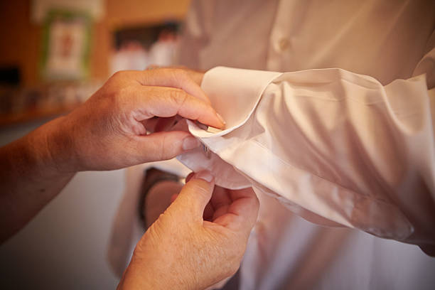 Hands of an elderly woman buttoning a man's cuff Close up of an elderly woman (presumably the mother) is helping a man (presumably a groom) getting dressed. She is buttoning the cuff of his shirt. Horizontal format. Shot with Canon EOS 5D. buttoning stock pictures, royalty-free photos & images