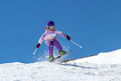 Smiling little girl on the high altitude ski slope in the Italian Alps. Happy little girl with helmet and ski goggles on the ski slopes.