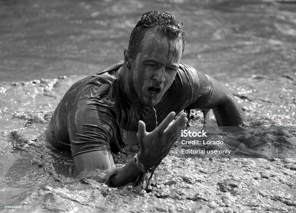 Male participant covered in mud at outdoor mud run event Biddinghuizen, The Netherlands - September 28th 2014: Male participant wading waist deep through a water and mud obstacle at the Mudmasters event on Sunday 28th September 2014 in Biddinghuizen, The Netherlands. Adversity Stock Photo