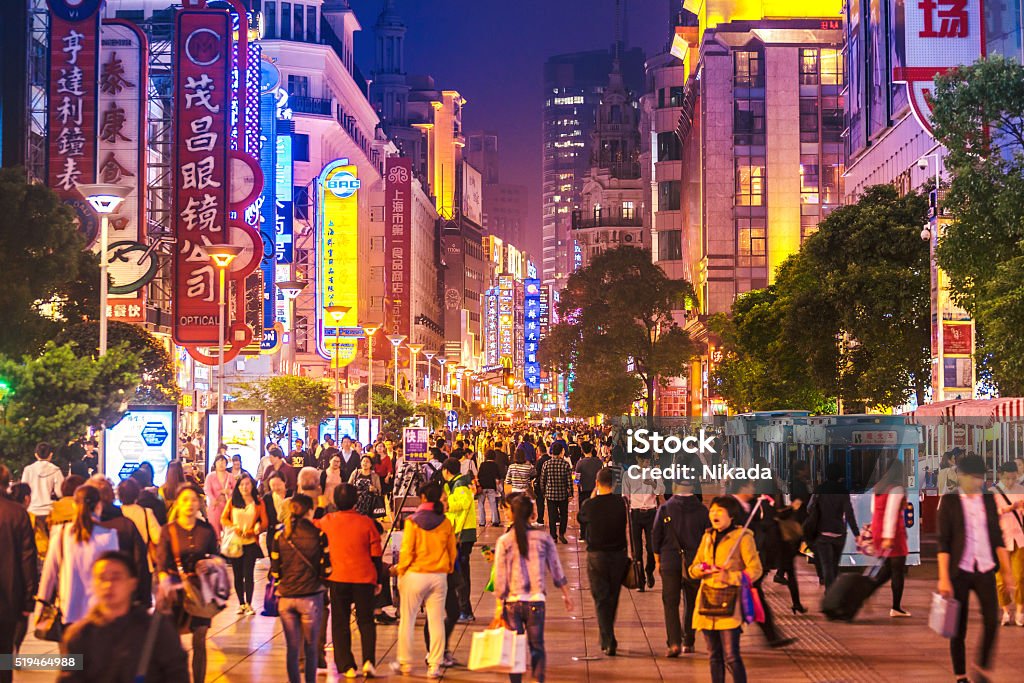 busy Shoppping Street in Shanghai, China at night Crowds walk below neon signs on Nanjing Road. The street is the main shopping district of the city and one of the world's busiest shopping districts.  China - East Asia Stock Photo