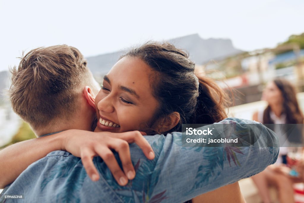 Young friends arriving at rooftop party Woman greeting her boyfriend and embracing. Young woman welcoming her friends at party. Young friends arriving at rooftop party. Embracing Stock Photo