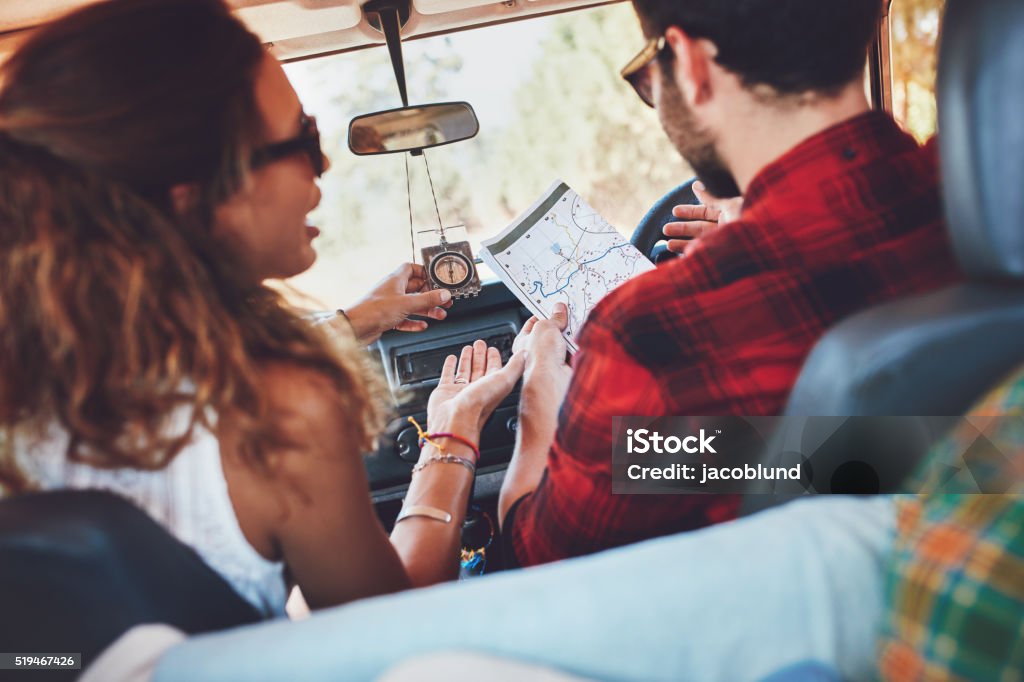 Couple using map to decide which way to go Rear view shot of a young couple on road trip reading a map and discussing while sitting in a car. Woman talking with her boyfriend in a car. Adult Stock Photo