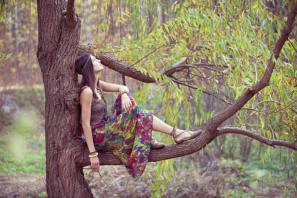 Teenage girl in headphones holding mobile phone and standing near tree on the background of forest