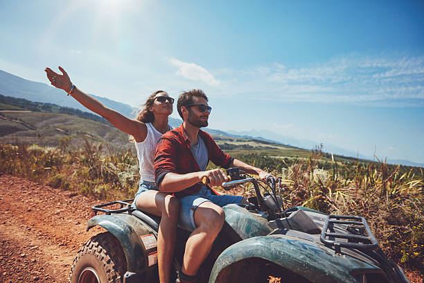 Young couple enjoying quad bike ride Happy young couple in nature on a quad bike. Young man and woman enjoying a quad bike ride in countryside. Man driving and woman enjoying the ride with her hands raised on a summer day. quadbike photos stock pictures, royalty-free photos & images