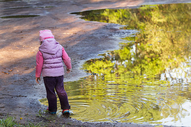 istock Back view of little girl exploring large spring puddle 519468640