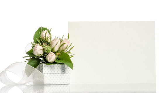 A box with white tulips and ornamental plants on a blue background, near the flowers is a white blank sheet of paper and an ink pen. Place for text.