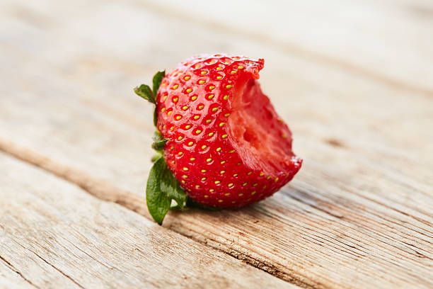 Fresh strawberry with one bite on wooden table