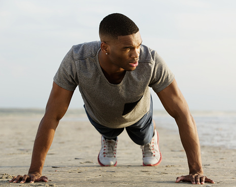 Portrait of an athletic young man doing push ups at the beach