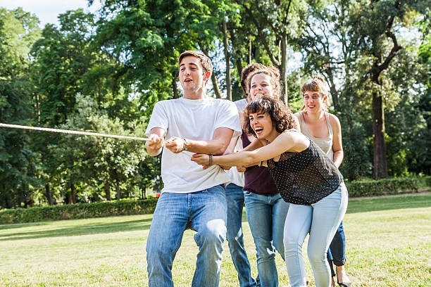 A large group of young people playing tug of war at the park in the summer.