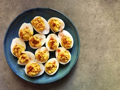 A plate of devilled chicken and duck eggs sprinkled with paprika and served on a blue stoneware/pottery plate,shot top down on a grey countertop background.