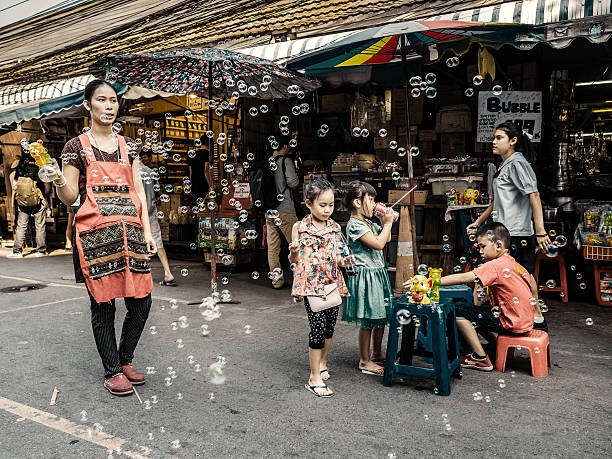 Bangkok, Thailand - February 28, 2016: Woman selling soap bubbles gun surrounded by playing children in Chatuchalk market. This weekend market in considered the biggest in Asia with more than 8000 stalls. It has been open since 1942 and is now located near the Mo Chit skytrain station.