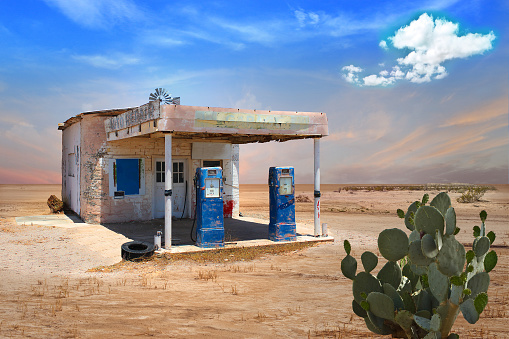 Old gas station with blue pumps in deserted arid landscape with a prickly pear cactus. Vintage look.