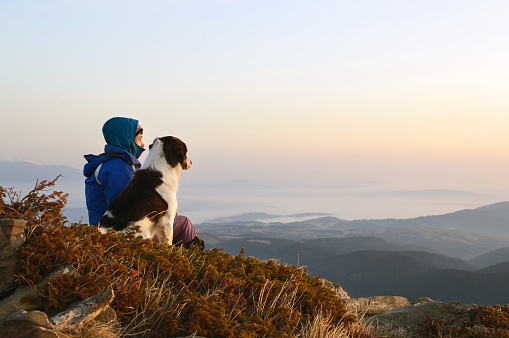 Young woman and dog admiring sunrise high in the mountain, Rila Mountains, Bulgaria