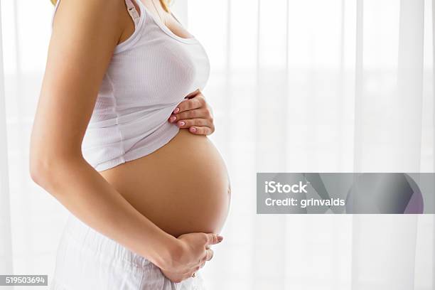 Pregnant Woman Standing Next To Window Stock Photo - Download Image Now - Pregnant, Women, Abdomen