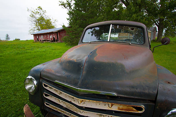 Midwest Scene: Rusty Green Pickup and Old Red Barn A Midwest USA scene: rusty green vintage pickup truck with shattered windshield in the foreground and an old red barn in the background, all on a carpet of bright green grass. distressed rusty vintage pickup truck close up detail stock pictures, royalty-free photos & images