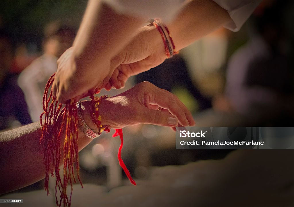 Indian Woman Receiving Sacred Thread Bracelet at Diwali Festival An Indian woman receives a traditional red and gold holy bracelet at an outdoor celebration during Diwali.  Jaipur, India. Raksha Bandhan Stock Photo