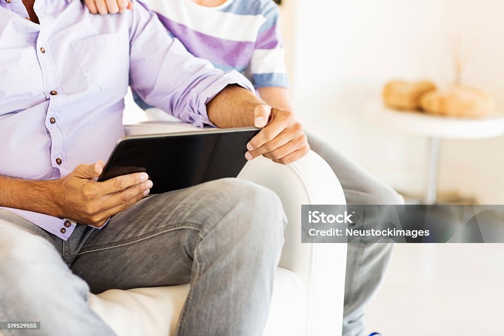 Father And Son With Digital Tablet At Home Midsection of father and son with digital tablet sitting on chair at home. Horizontal shot. 10-11 Years Stock Photo