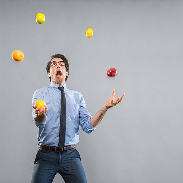 Out of Control Nerdy Businessman Juggeling Fruits Nerdy caucasian businessman mid thirties, wearing a blue shirt and tie. He looks out of control an panicked while juggling two apples, a pear, oranges and a lemon. Shot in the studio on a grey background with the Nikon D800. juggling stock pictures, royalty-free photos & images