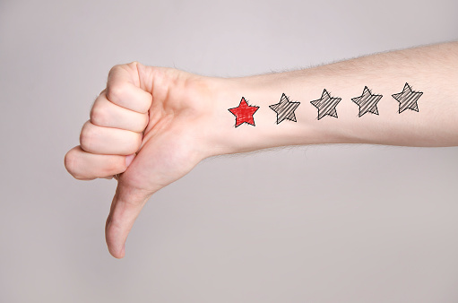 Closeup of man hand showing thumb down on gray background and one star rating on the arm skin. Dislike concept 