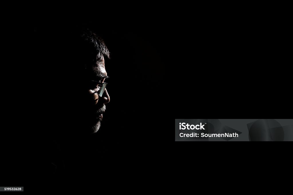 Portrait of a senior man in dark background. Portrait of a senior man wearing glasses. Very dramatic lighting in this image. The background is jet black. Men Stock Photo