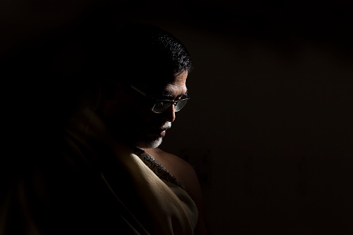 Portrait of a senior man wearing glasses. Very dramatic lighting in this image. The background is jet black.