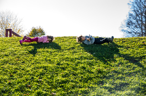 Two kids rolling down a grass hill