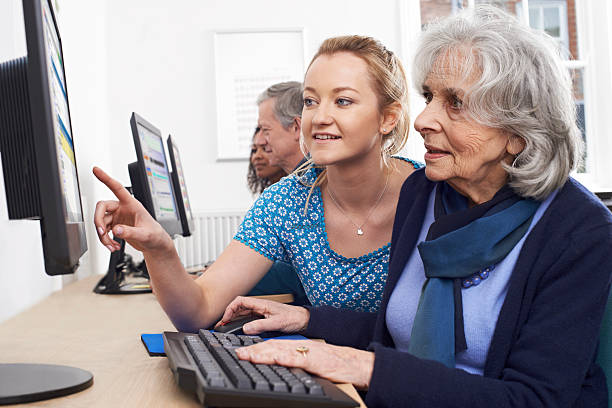 nachhilfelehrer helfen senior frau in computer-klasse - computeranlage stock-fotos und bilder