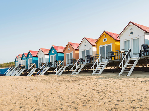 Sandy beach with colorful beach cabanas with white stairs in a row.