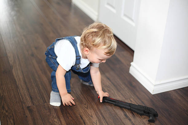 Little boy picking up a gun Little boy squatted and picking up a gun from the floor. Toy-gun and little boy. Child proofing. Danger of fire arms at home. baby gun stock pictures, royalty-free photos & images