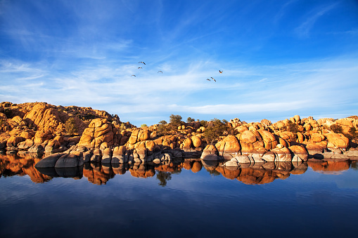 Beautiful red rock mountains reflecting in the water along the shore of Watson Lake in Prescott, Arizona, USA.