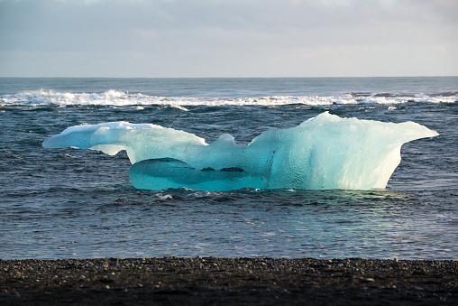 Huge blue iceberg in the ocean, black sand beach at Jokulsarlon, winter, Iceland