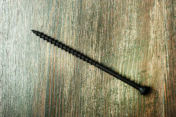 Black screw on wooden background, macro shot