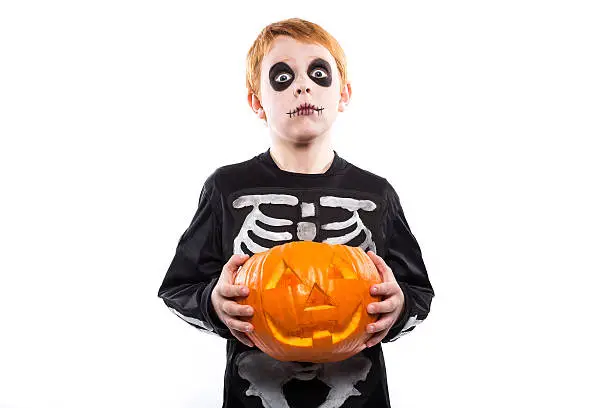 Photo of Red haired boy in skeleton costume holding a pumpkin. Halloween
